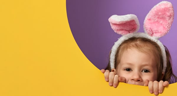 Little Girl in a bunny costume peaking out from a circular opening in a bright yellow wall